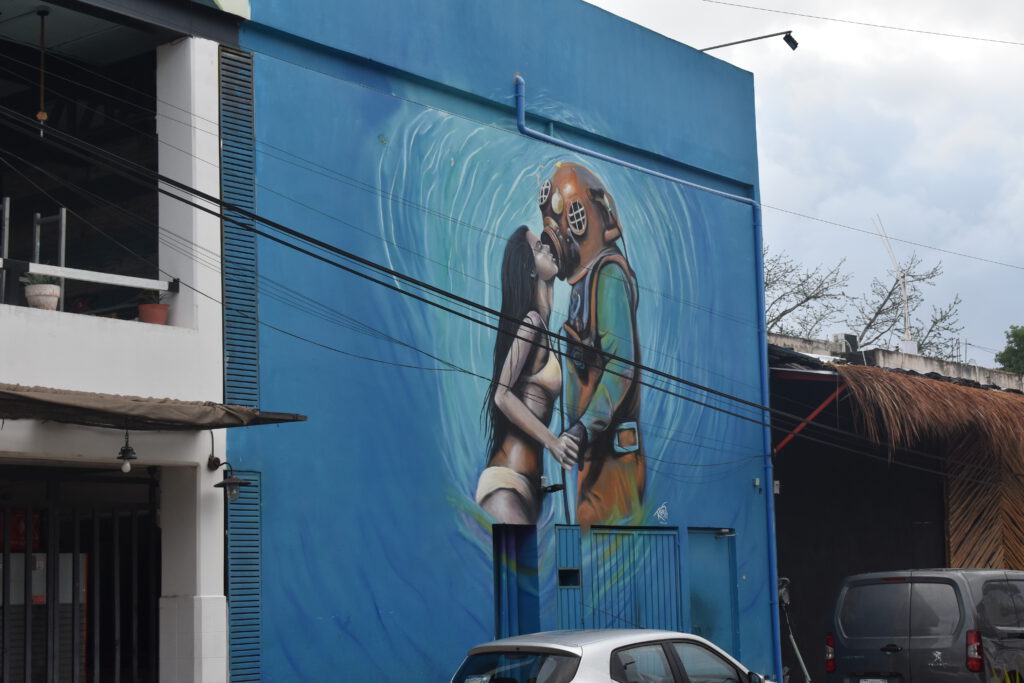 Buntes Kunstwerk an einem Haus in Tulum. Es zeigt eine Frau im Bikini, die einen Astronauten küsst.