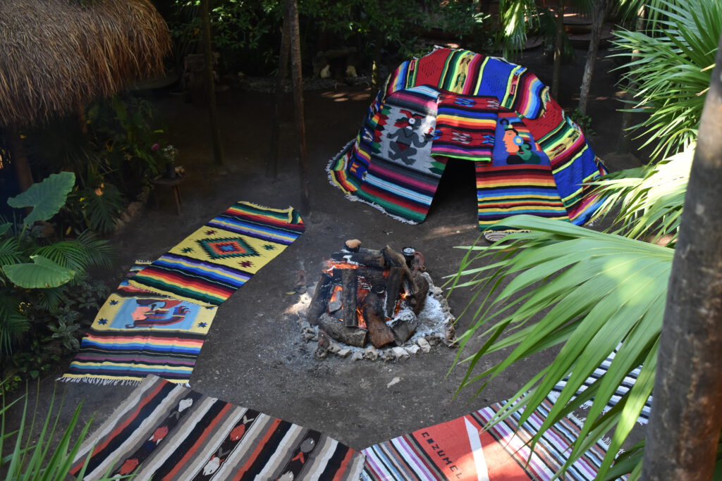 Mit bunten Textilien abgedecktes Temezcal-Zelt vor einem Lagerfeuer